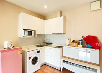 Small kitchen with white cabinets, a washing machine, microwave, and a pink refrigerator
