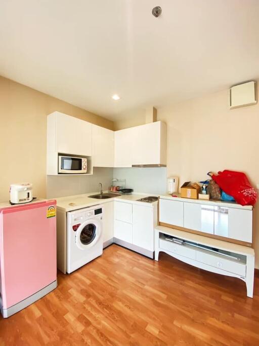 Small kitchen with white cabinets, a washing machine, microwave, and a pink refrigerator