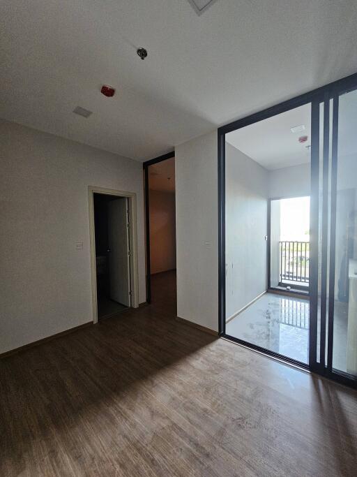 A room with wooden flooring and a sliding glass door leading to a small balcony