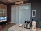 Well-lit living room with sheer curtains, air conditioner, TV, and kitchen appliances