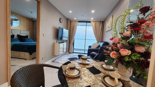 Modern living room with adjacent bedroom, featuring a dining area and ocean view