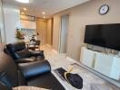 Modern living room with black leather sofa, wall-mounted TV, and view into kitchen