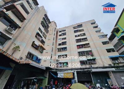 Exterior view of a multi-story residential building with shops and parking area