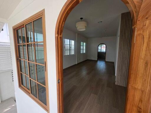 View through an arched doorway into a spacious room with wooden flooring and large windows