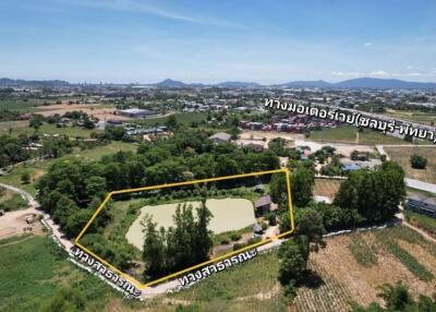 Aerial view of a land plot surrounded by greenery with nearby roads and rural landscape.