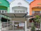 Front view of colorful row houses with a covered parking area and a gate