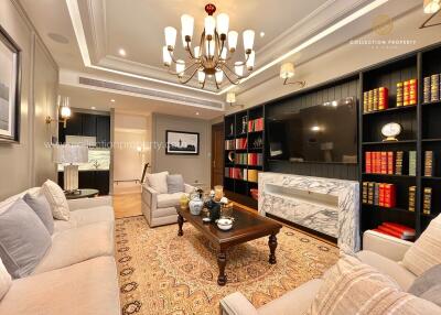 Elegant living room with comfortable seating, chandelier, bookshelf, and marble fireplace