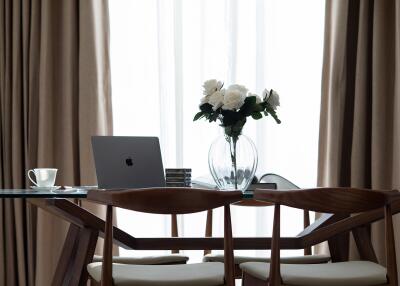 Dining area with glass table, chairs, laptop, and flower vase.