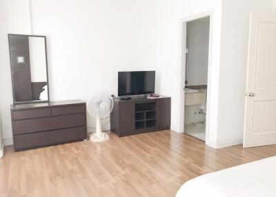 A bedroom with wooden flooring, dresser, mirror, fan, TV, and an attached bathroom