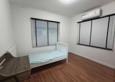 Simple bedroom with a single bed, wooden desk, and air conditioner