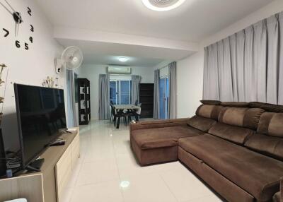 Modern living room with brown sectional sofa, large flat-screen TV, dining area, and wall clock.