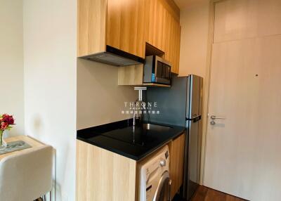 Compact modern kitchen with wooden cabinets, microwave, fridge, and washing machine