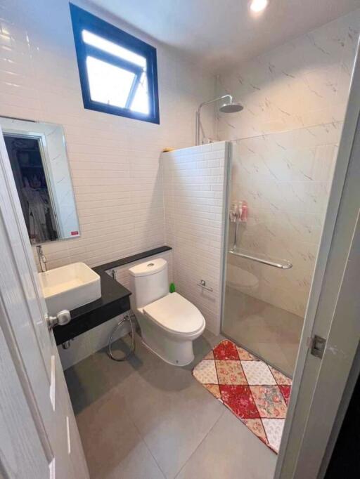 Modern bathroom with glass-enclosed shower, sink, toilet, and window