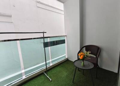 Small balcony with artificial grass, a chair, and a table with flowers