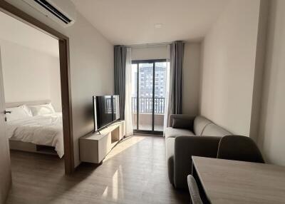 Modern living room with television, sofa, and a view of the balcony, adjacent to a bedroom