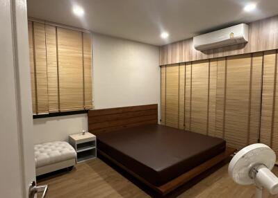 Modern bedroom with wooden bed frame, white ottoman, and air conditioning