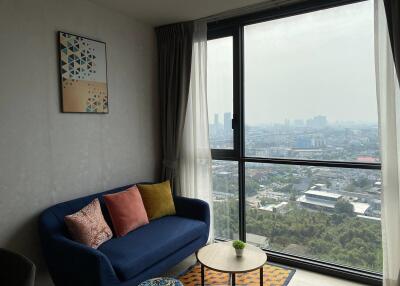 A cozy living room with a blue couch and a large window overlooking a cityscape