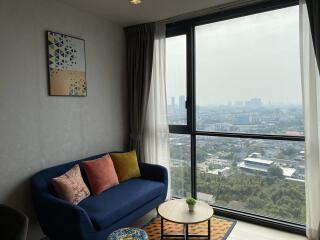 A cozy living room with a blue couch and a large window overlooking a cityscape