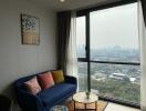 A cozy living room with a blue couch and a large window overlooking a cityscape