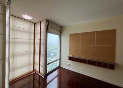 A bedroom with parquet flooring, large windows with blinds, and a wall-mounted shelf.