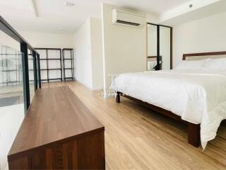 Spacious bedroom with wooden flooring, large bed, and modern furnishings