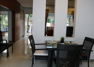 Dining area with a dining table and chairs, adjacent to a hallway with a view of greenery outside