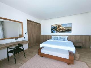 A modern, stylish bedroom with a large bed, artwork on the wall, a wooden desk with a mirror, and a chair.