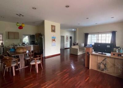 Spacious living area with wooden flooring, dining set, kitchen area, and television