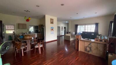 Spacious living area with wooden flooring, dining set, kitchen area, and television