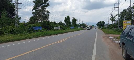 Photo of a paved road with vehicles and surrounding greenery