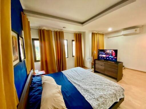 Modern bedroom with a large bed, television, chest of drawers, and yellow curtains