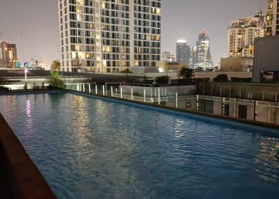 Outdoor swimming pool with city view and nearby tall buildings at night