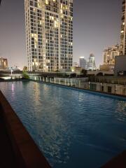 Outdoor swimming pool with city view and nearby tall buildings at night