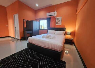 Spacious bedroom with orange walls, double bed, bedside lamp, vanity table, and air conditioner.