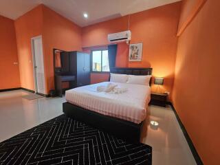 Spacious bedroom with orange walls, double bed, bedside lamp, vanity table, and air conditioner.