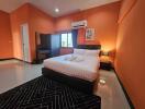 Spacious bedroom with orange walls, double bed, bedside lamp, vanity table, and air conditioner.