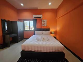 Modern bedroom with orange walls, a double bed, wardrobe, and air conditioning unit