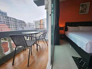 Balcony with a table and chairs overlooking buildings, adjacent to a bedroom