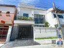 Modern two-story white house with a balcony and gated entrance