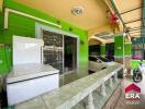 Covered outdoor space with green walls, tile flooring, a white refrigerator, and cars parked nearby