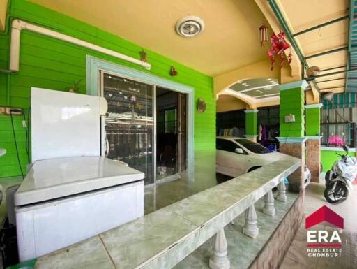 Covered outdoor space with green walls, tile flooring, a white refrigerator, and cars parked nearby