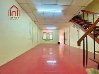 Spacious open living area with red tiled flooring, stairway access, and ample lighting