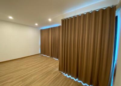 Spacious living area with wooden flooring and large windows covered by brown curtains