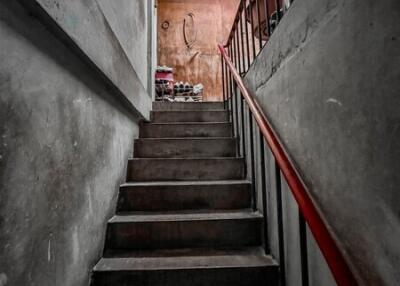 A dark concrete staircase with a red handrail leading upstairs.