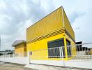 Exterior view of a modern yellow building with a white fence