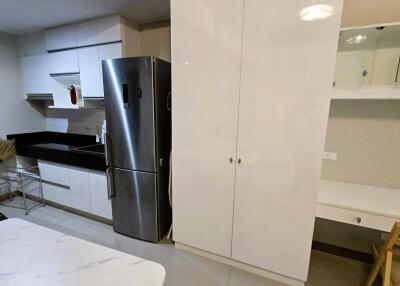 Modern kitchen with white cabinets, stainless steel refrigerator, and black countertops.