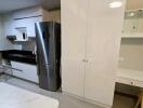 Modern kitchen with white cabinets, stainless steel refrigerator, and black countertops.