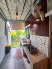 Outdoor covered kitchen with tiled flooring, sink, stove, fan, and garden view