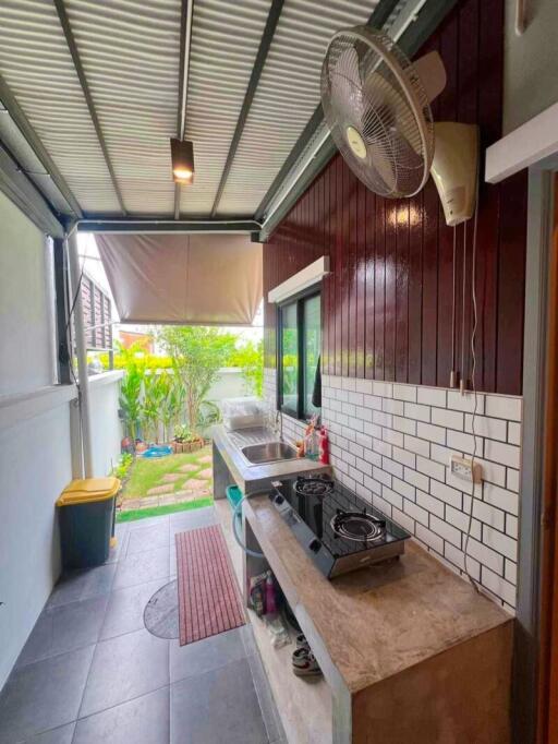 Outdoor covered kitchen with tiled flooring, sink, stove, fan, and garden view