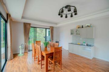 Bright dining area with wooden flooring, modern light fixture, sliding glass doors, and adjacent kitchenette